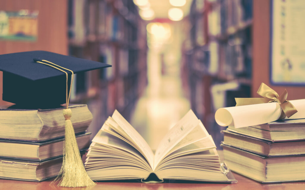 A graduation cap, open book and diploma, and all the research that accompanies a doctorate